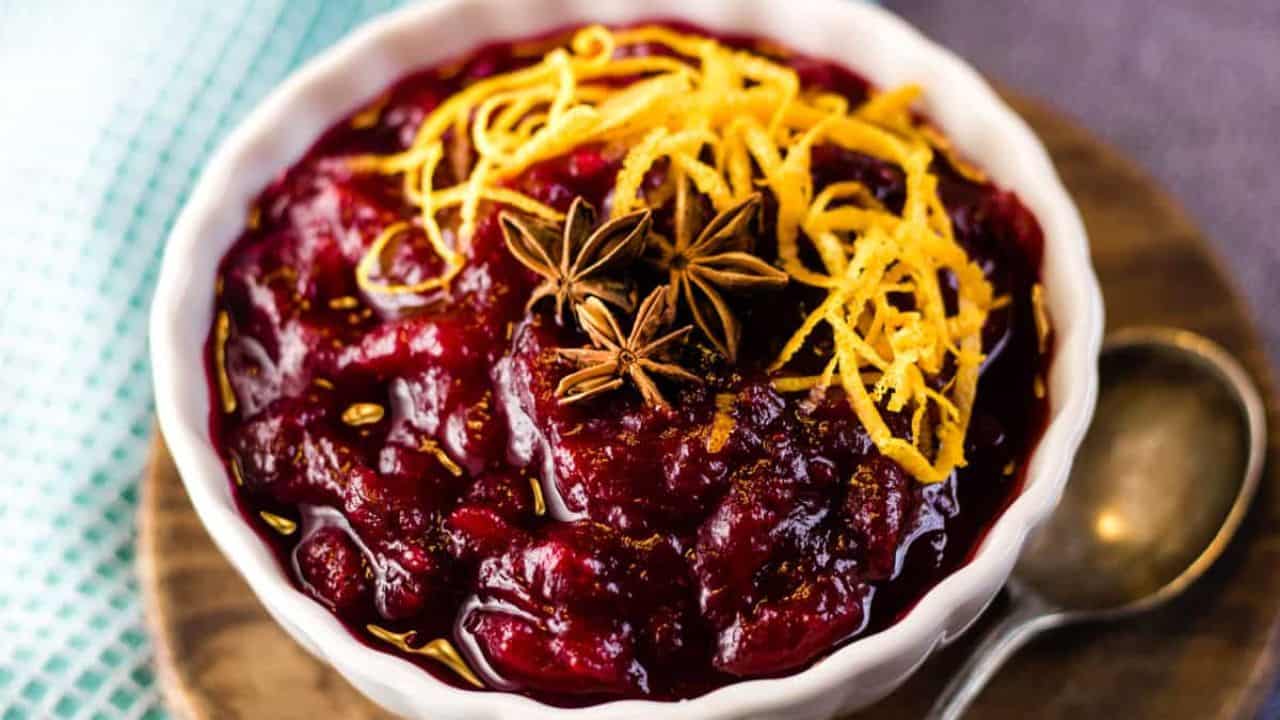 Cranberry sauce in a white bowl garnished with orange zest and star anise pods.