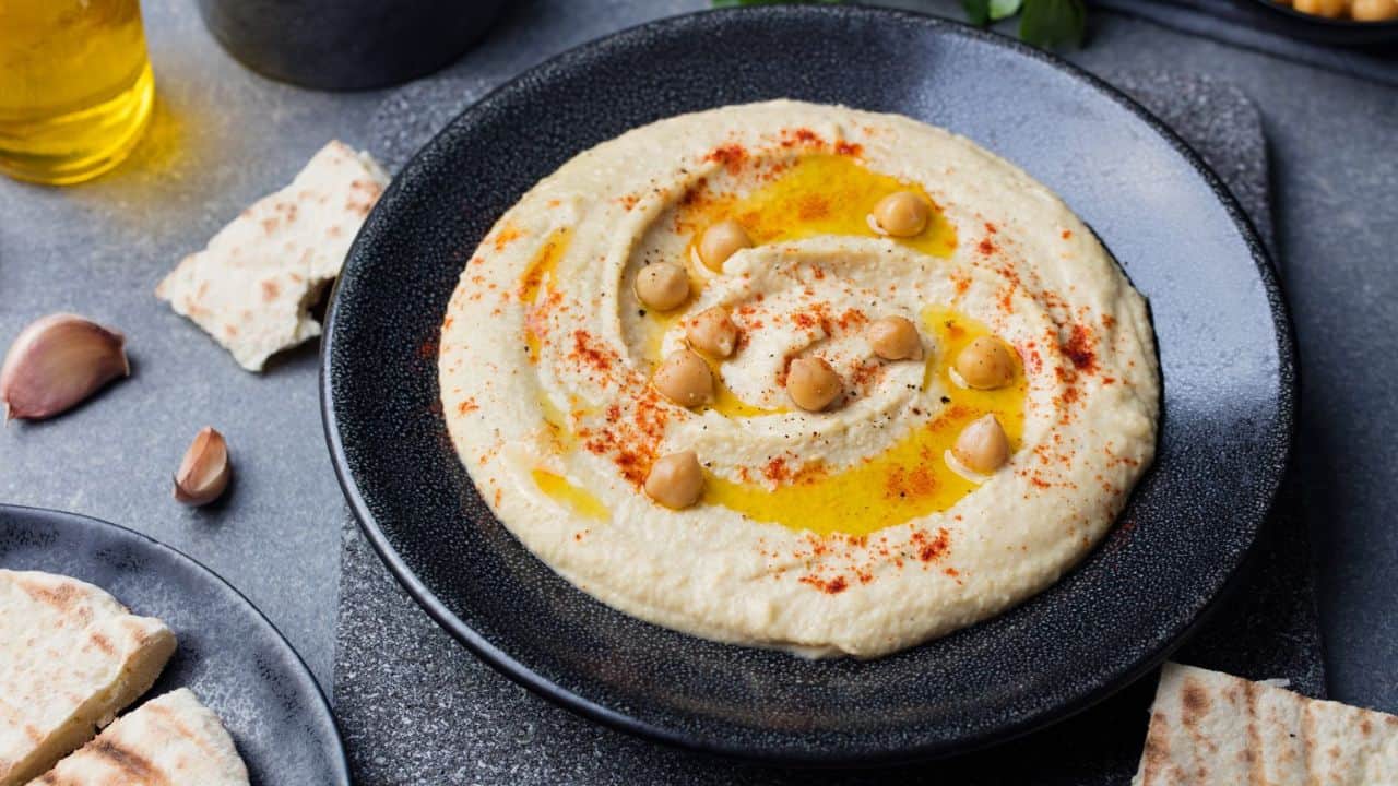 Hummus in a black bowl garnished with whole chickpeas, olive oil, and paprika.