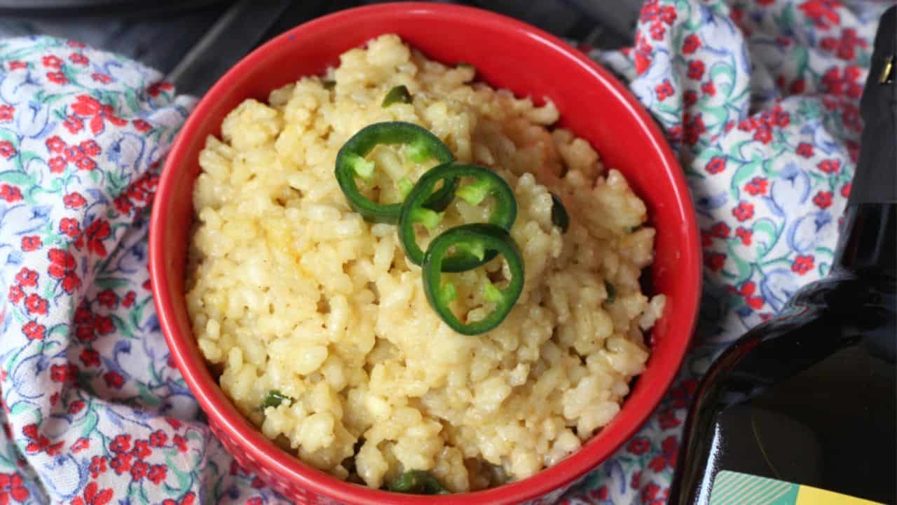 Red bowl of risotto topped with sliced jalapeños.