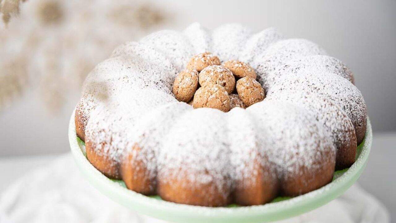 A bundt cake dusted with powdered sugar is displayed on a stand, with small round cookies arranged in the center.