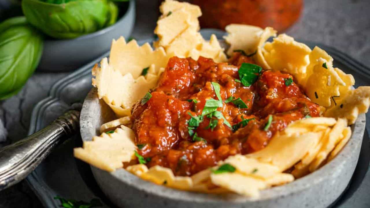 Pasta Marinara inside a grey plate with extra sauce and basil leaves on the side.
