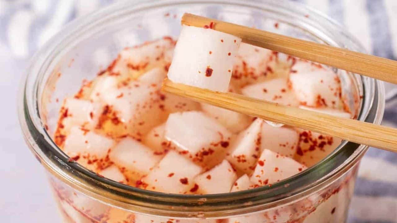 A close-up of a glass jar filled with small, cubed pieces of radish, seasoned with red chili flakes.