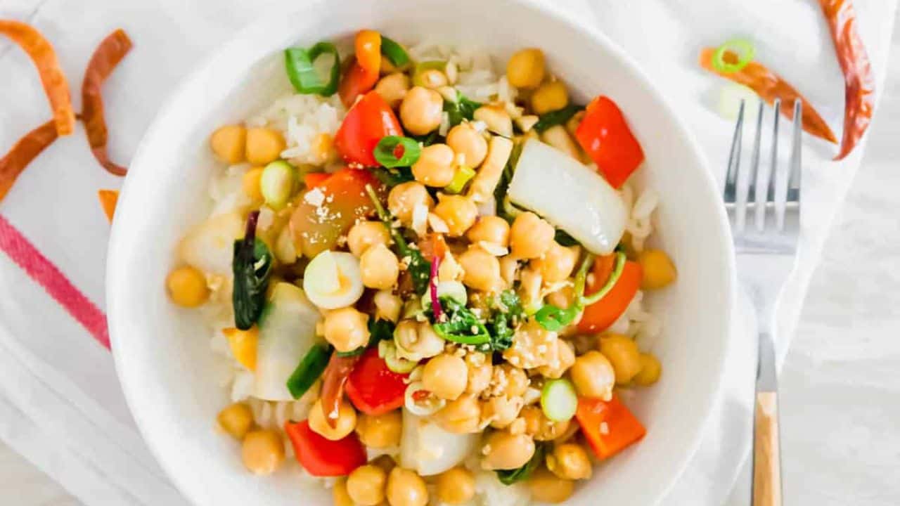 Kung pao chickpea dish in a bowl with rice and skillet off to the left.