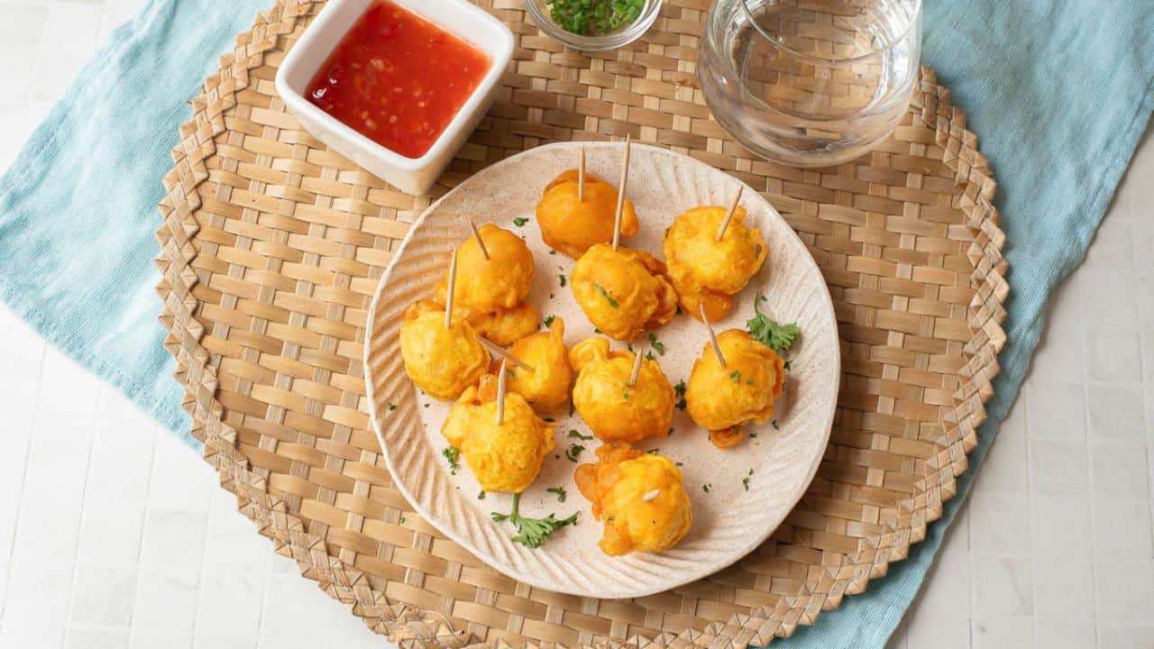 A plate with several orange-colored, bite-sized snacks on toothpicks, some cut open to reveal an egg inside, topped with a red sauce and garnished with herbs.
