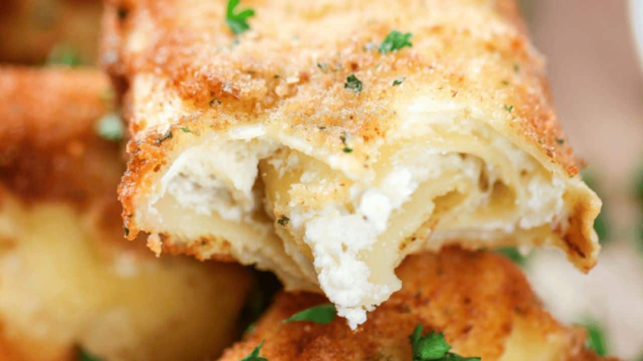 Close-up of a breaded, fried pasta roll filled with ricotta cheese, garnished with small pieces of parsley.