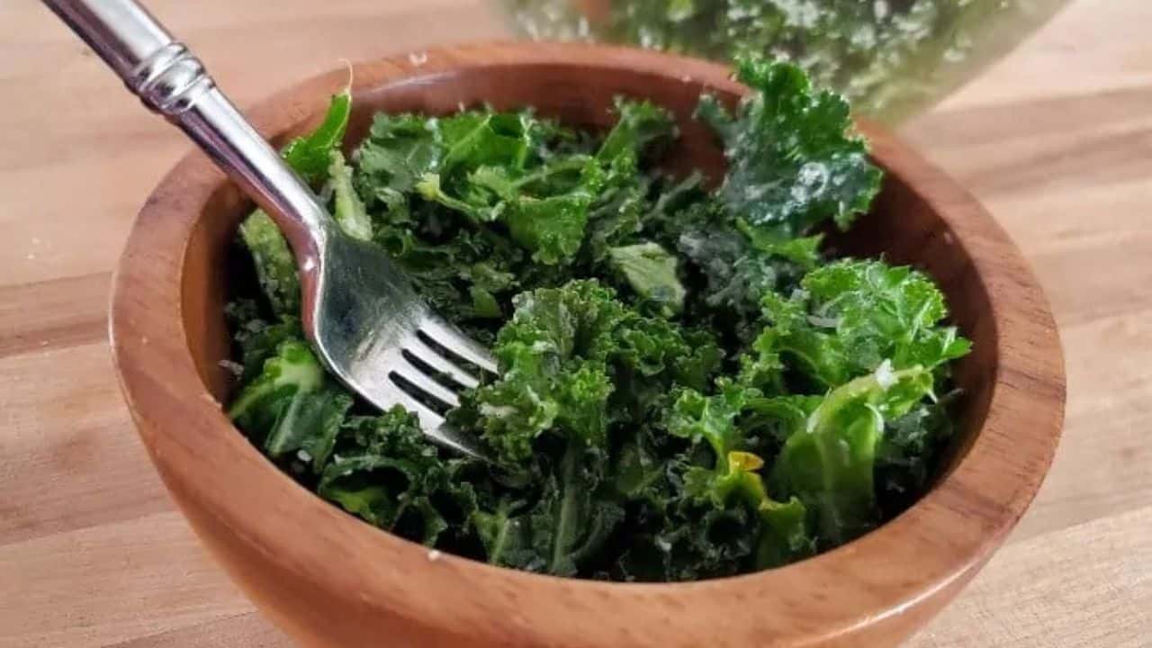 Image shows a fork holding a bite of lemon kale salad with the full bowl behind it.
