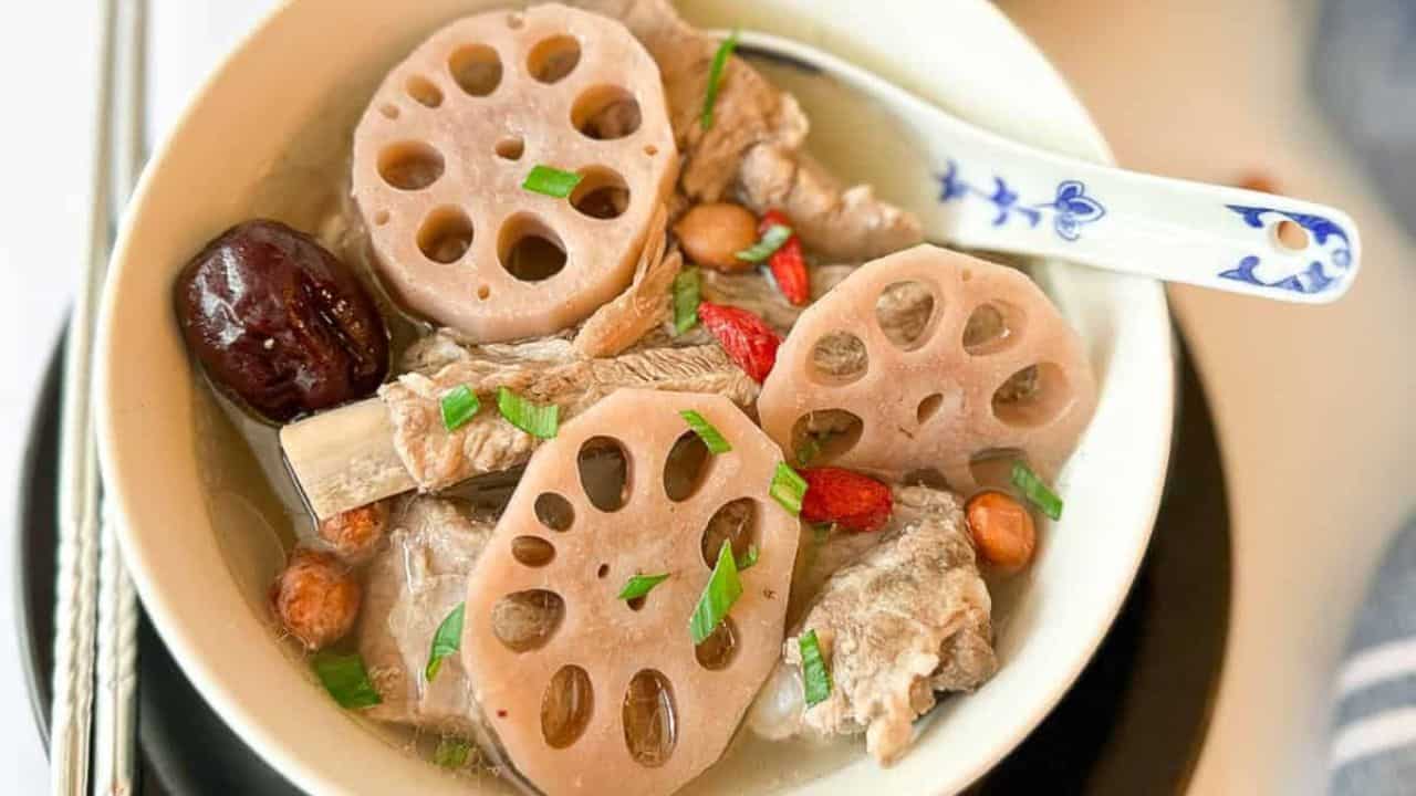 A bowl filled with pork ribs and lotus roots and a pair of chopsticks resting on the side.