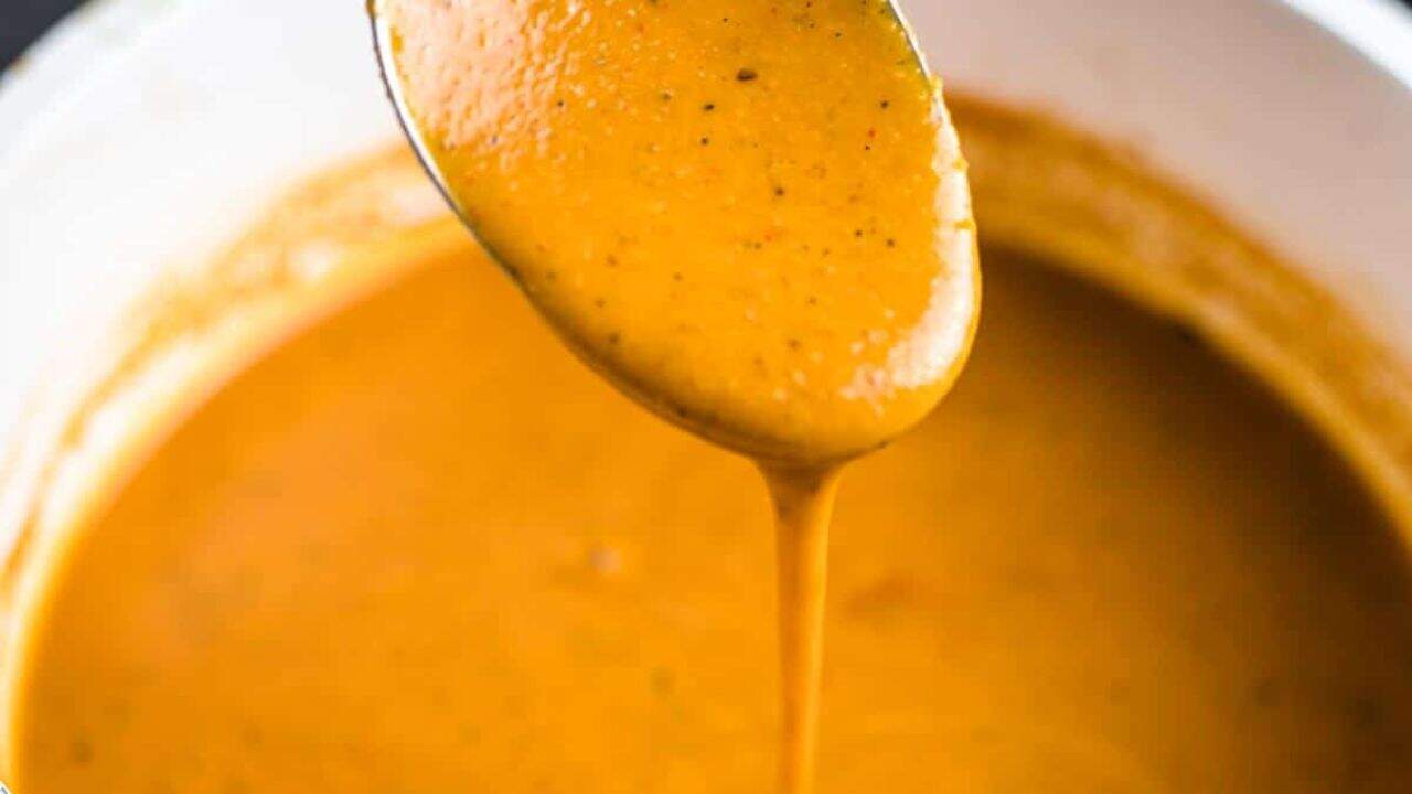 Enchilada sauce in a glass container with a spoon dishing it up.