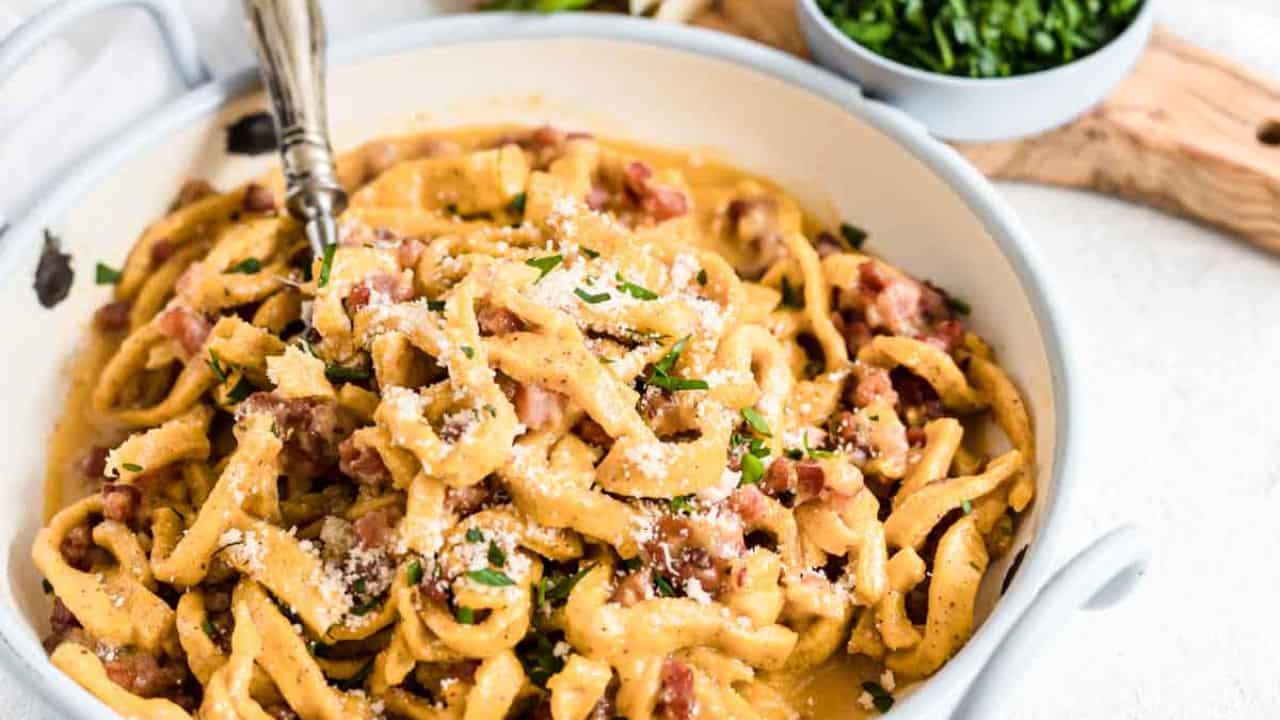 Pasta Carbonara inside a bowl with herbs and bacon.