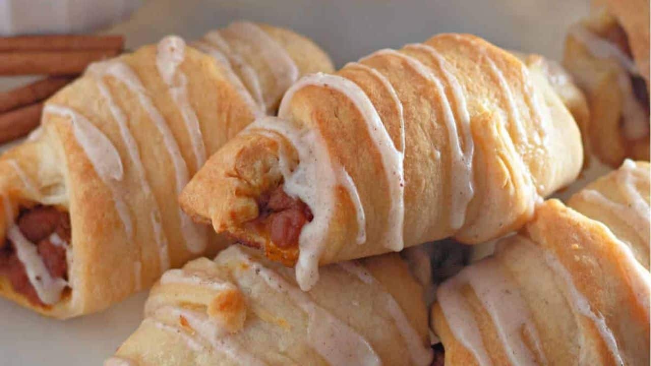 Mini pumpkin crescent rolls with dipping sauce on a plate.