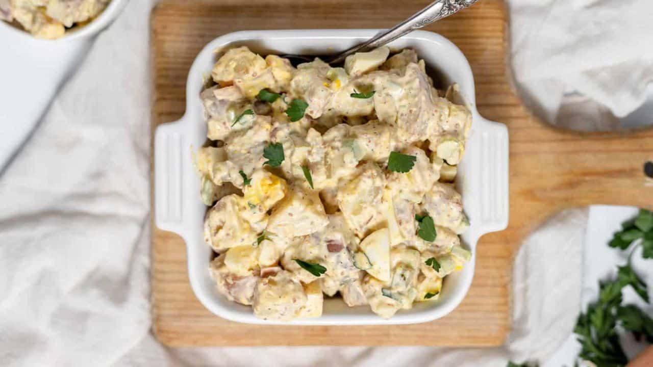 A close-up of mustard potato salad in a white dish, garnished with fresh herbs.