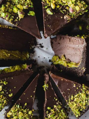 Six slices of chocolate cake with a green filling and sprinkled with crushed pistachios, arranged in a circle on parchment paper.