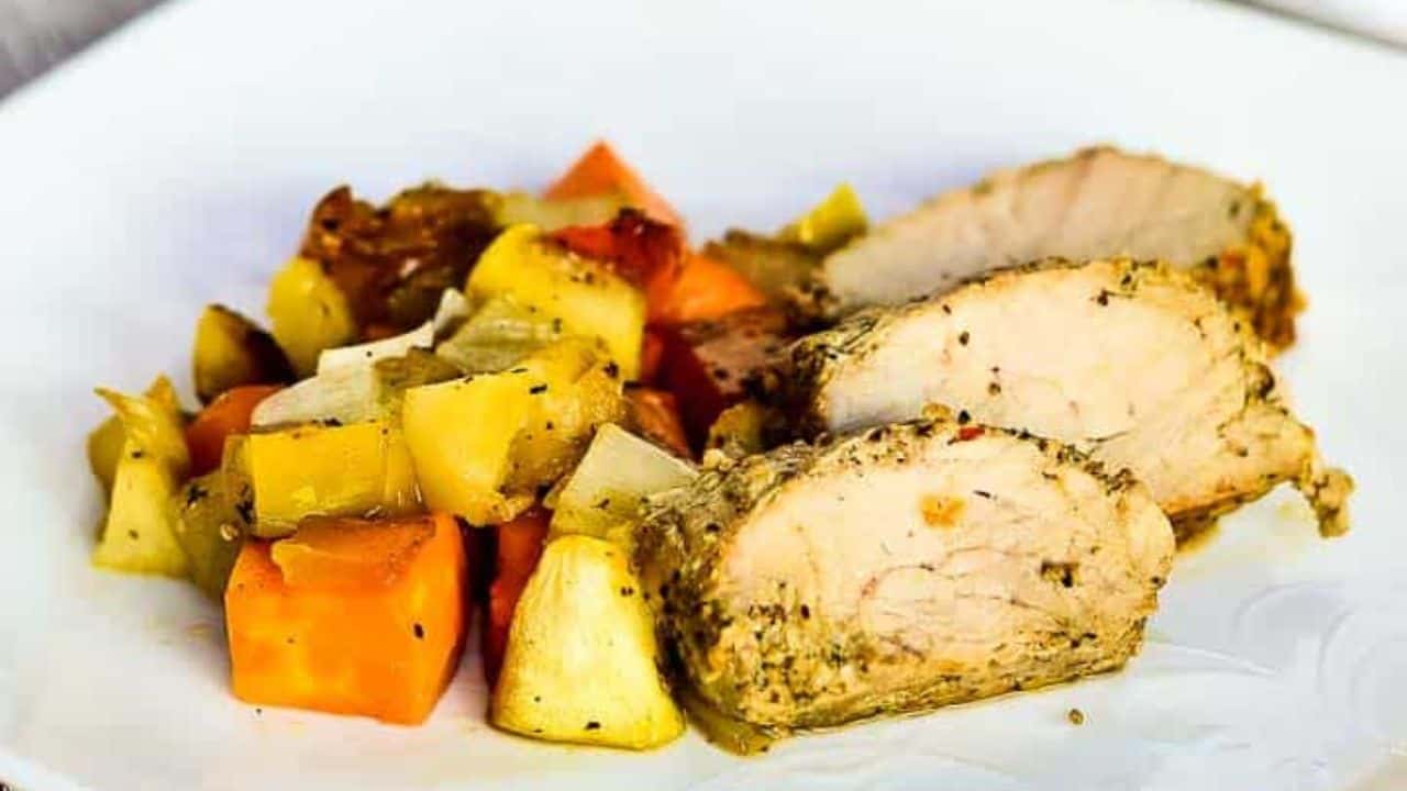 Cooked seasoned pork surrounded by diced vegetables in a black skillet on a wooden table.