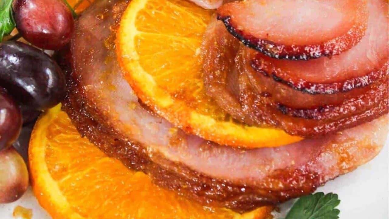 Sliced ham with orange slices and grapes, garnished with parsley on a platter.