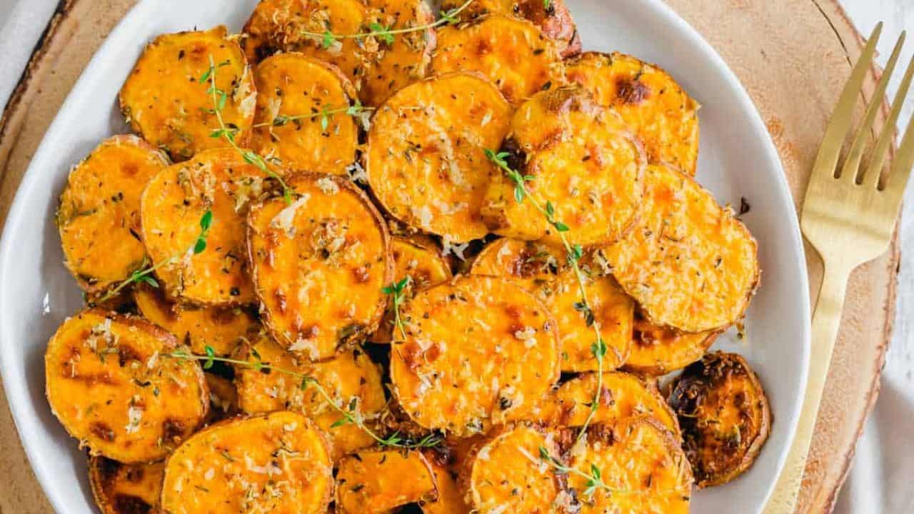 Air fryer sweet potato rounds with a parmesan herb crust garnished with thyme sprigs on a plate.