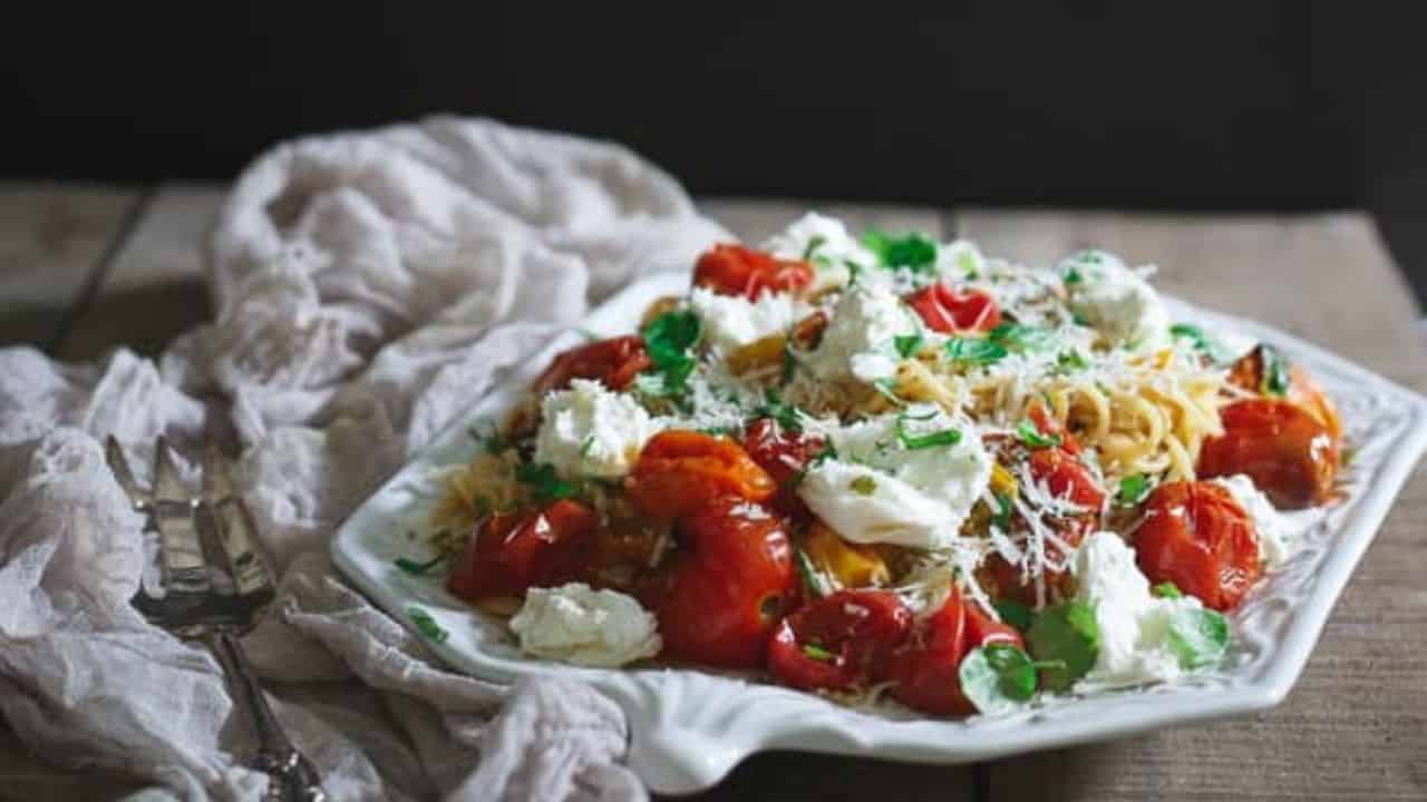 Pasta Checca with burst tomatoes and burrata on a white serving platter.