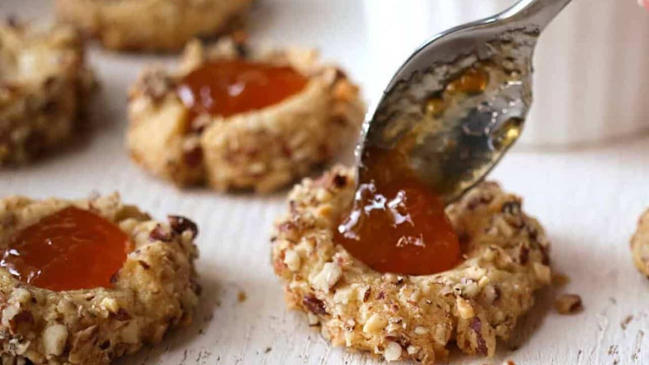 Spooning apricot jam into pecan thumbprint cookies.
