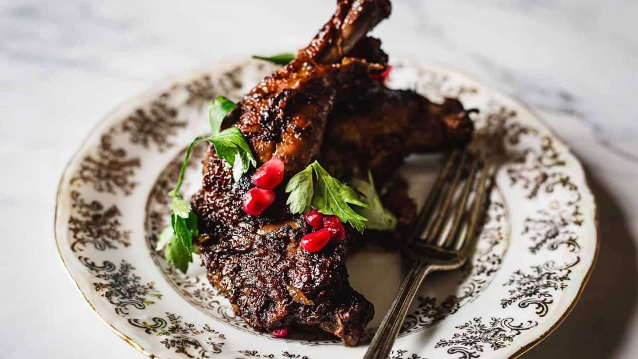 A close-up image of a slow-cooked meat dish garnished with fresh parsley and pomegranate seeds served in a rustic pot.