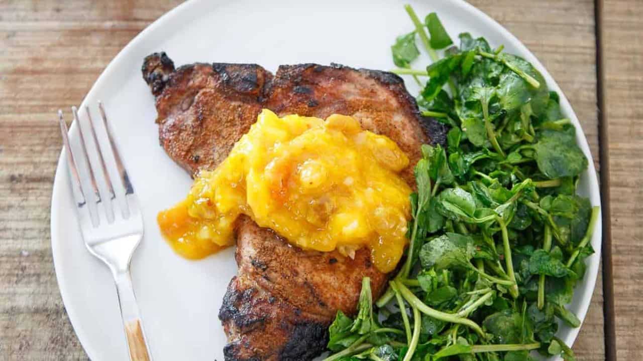 Spice rubbed grilled pork chops topped with mango peach chutney on a white plate.