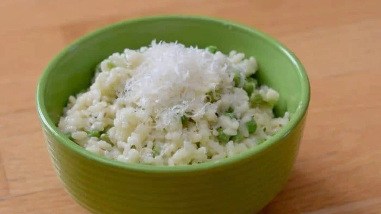 Image shows a Spoonful of risotto with peas and lemon with the rest of the bowl in the background.