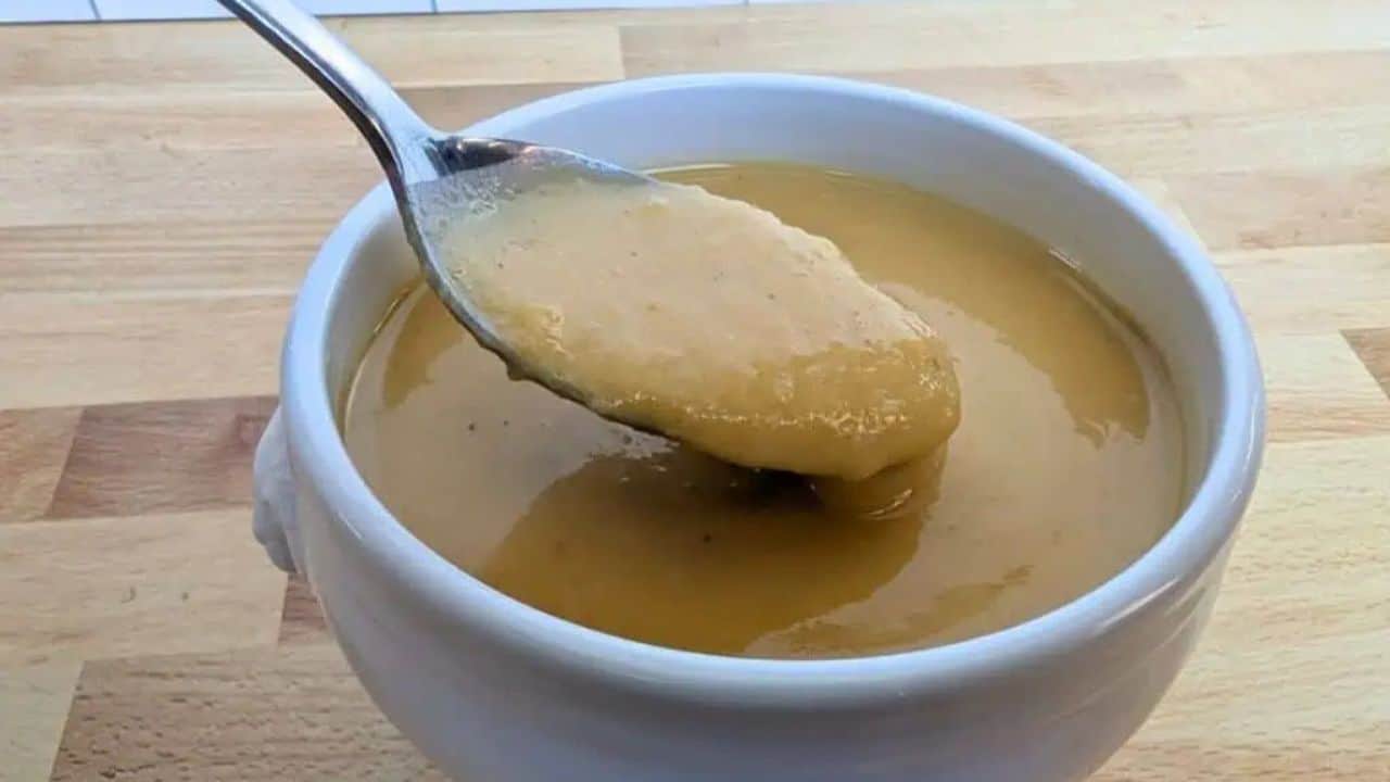 A spoonful of thick, creamy soup being lifted from a white bowl placed on a wooden surface.