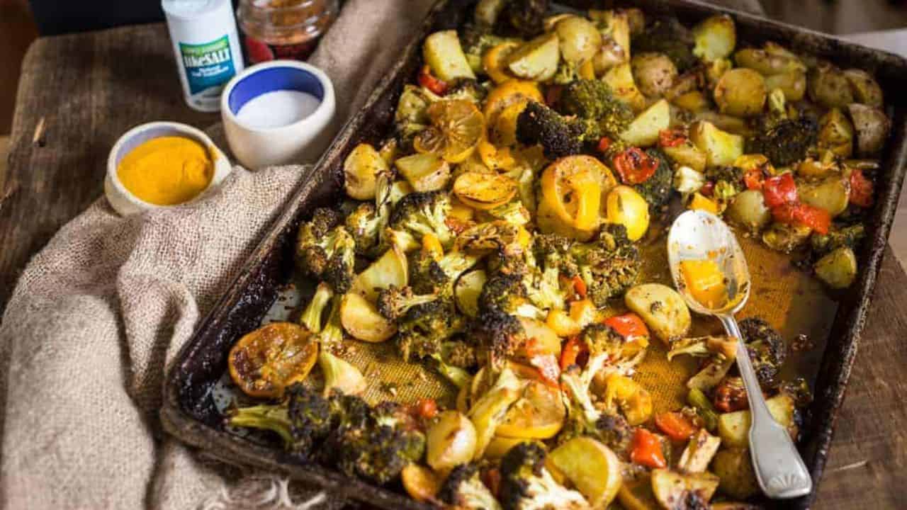 Roasted vegetables and lemon slices on a baking sheet, with a spoon and small bowls on the side.