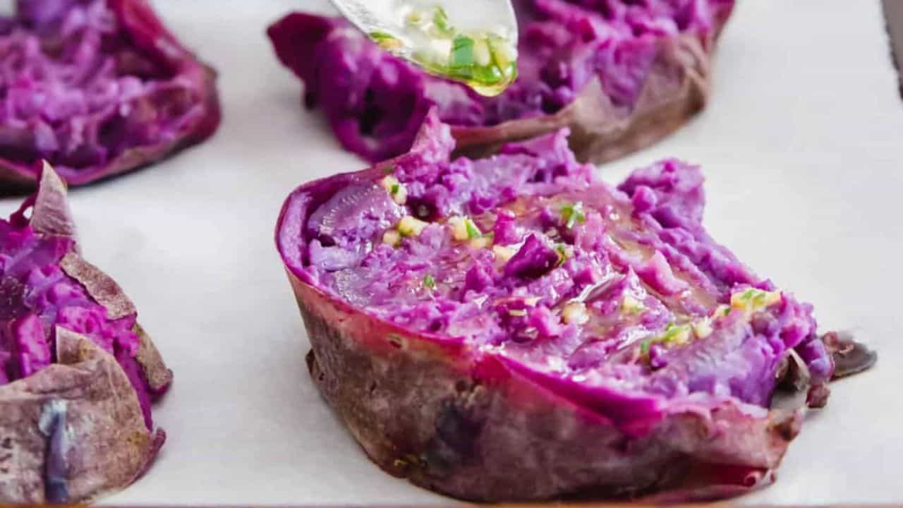 Smashed roasted purple sweet potatoes on parchment paper lined baking sheet.