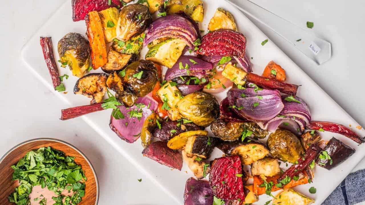 An overhead image of roasted vegetable salad on a serving dish. with the dressing on the side.