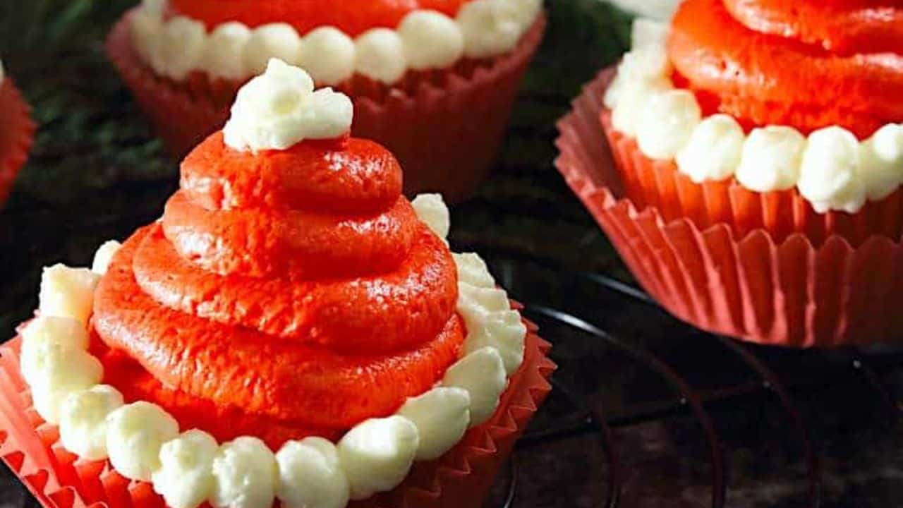 Cupcakes decorated with red and white frosting to resemble Santa hats, placed in red paper liners.