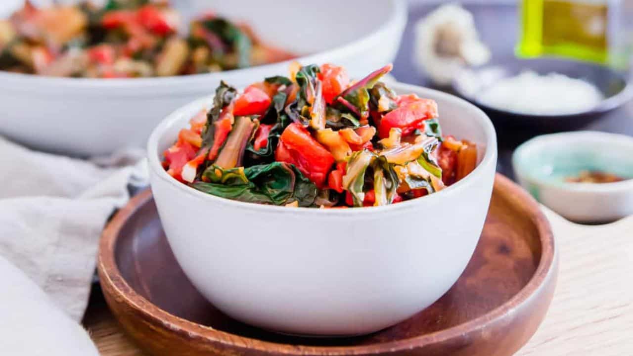 Sautéed Swiss chard in a white skillet with wooden serving spoon.