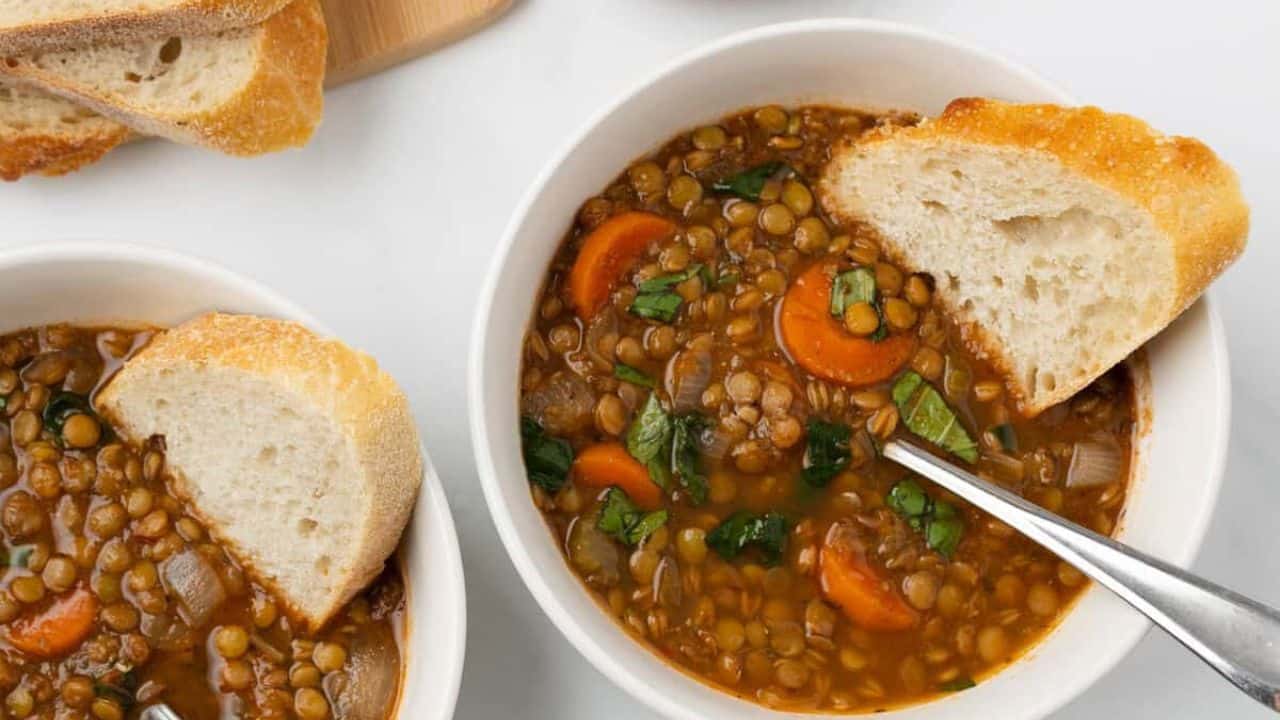 A bowl of slow cooker lentil soup with a slice of bread and a spoon.