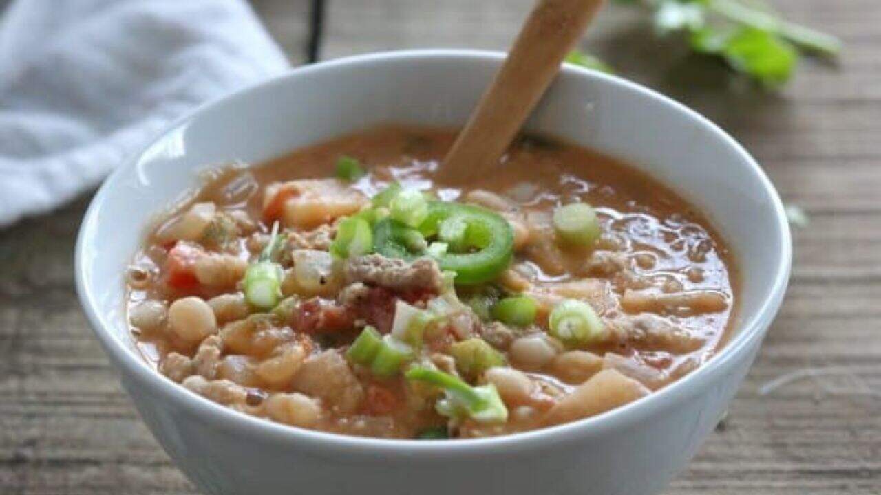 A skillet full of meat and beans in a pan with a wooden spoon.