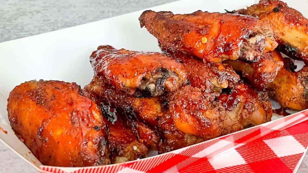 A white tray filled with several glazed and seasoned chicken wings sits on a red and white checkered surface.