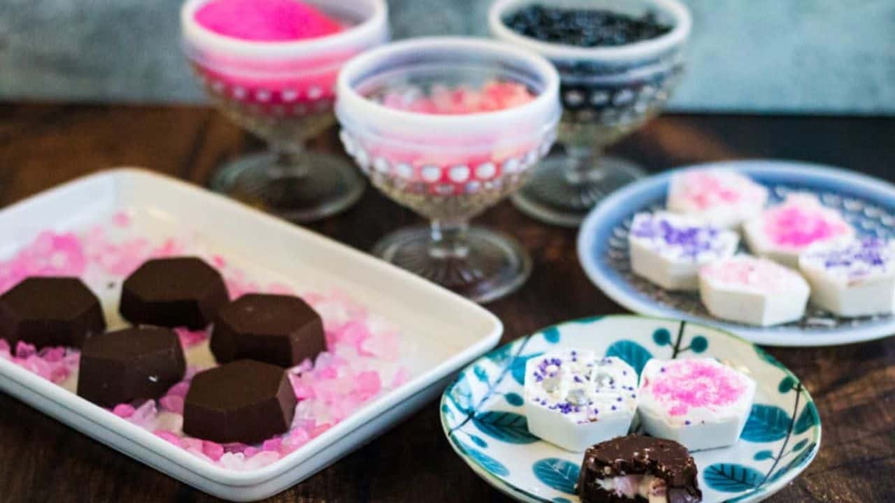 Chocolate covered strawberry cheesecake bites on little plates with pink sprinkles.