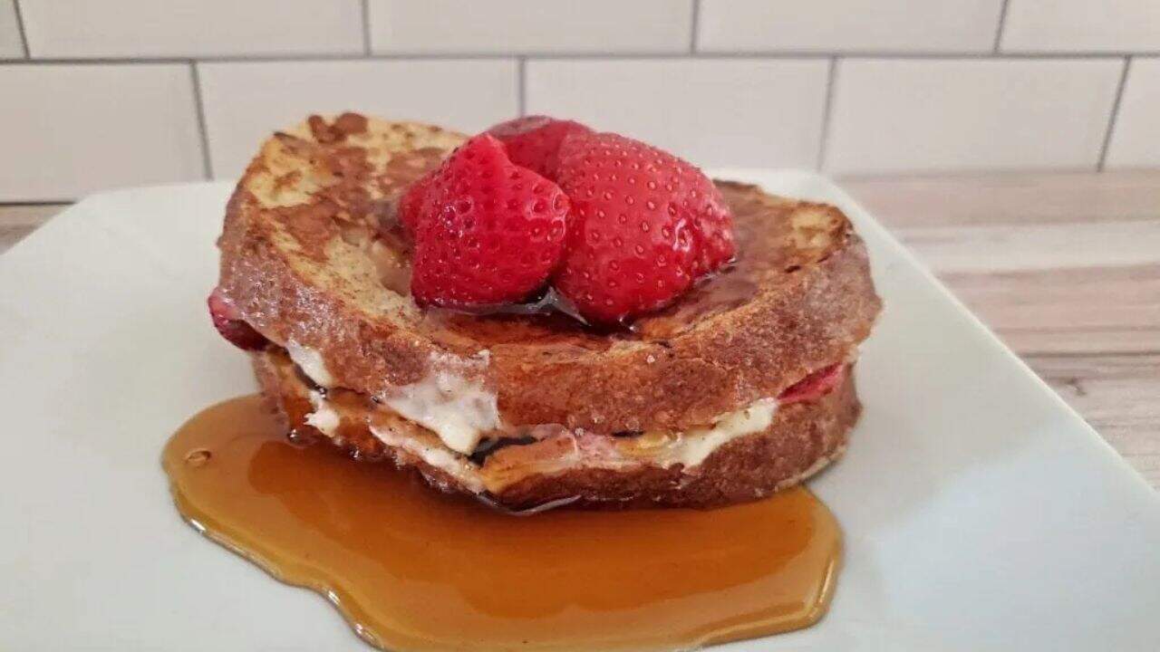 Image shows Strawberry Stuffed French Toast on a white plate with syrup around it.