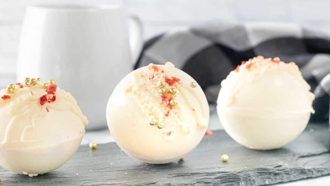 A person holding a Strawberry White Chocolate Cocoa Bomb with sprinkles on it.