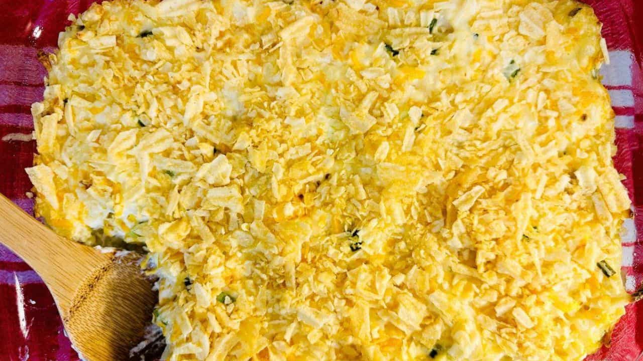 A casserole dish with shredded cheese and a wooden spoon.
