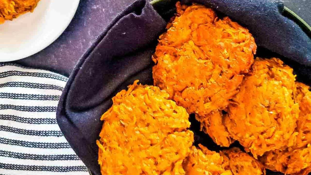 A serving basket of sweet potato fritters next to a bowl of dipping sauce and a single serving on a plate.
