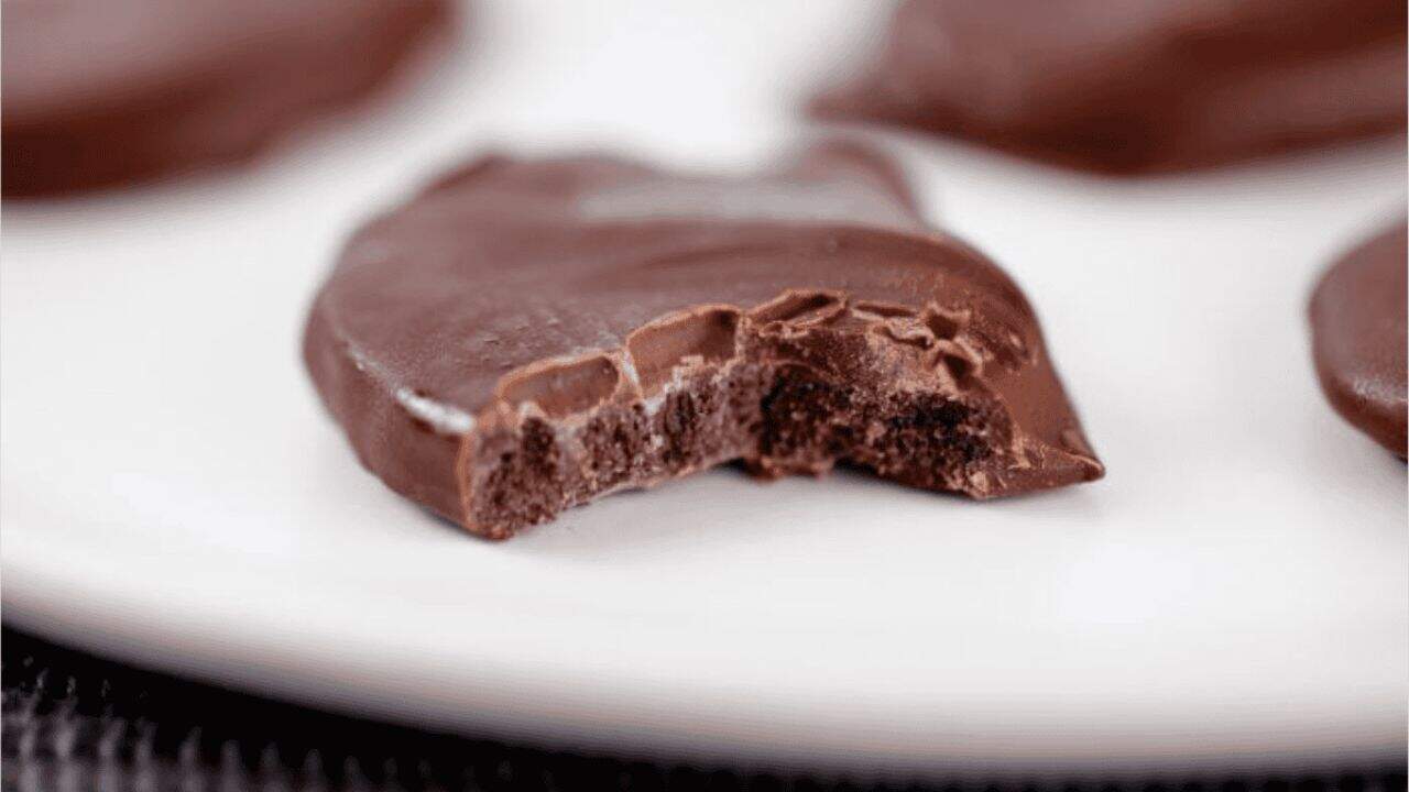 A chocolate-covered cookie with a bite taken out is shown on a white plate, with other whole cookies in the background.
