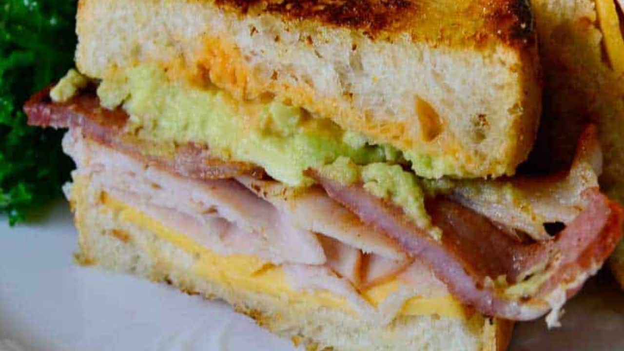 Two slices of turkey avocado club sandwich on a white plate.