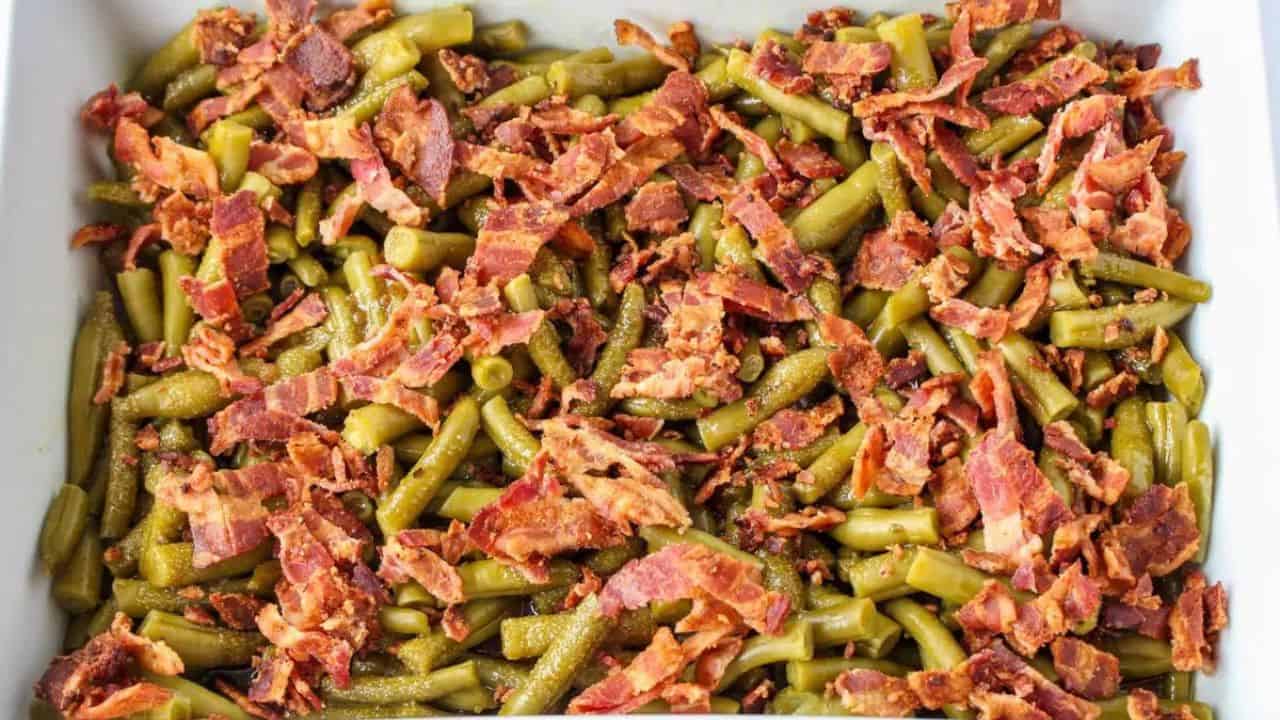 A white baking dish filled with cooked green beans mixed with crispy bacon pieces.