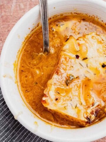 A bowl of French onion soup topped with melted cheese and bread, with a spoon resting inside the bowl.