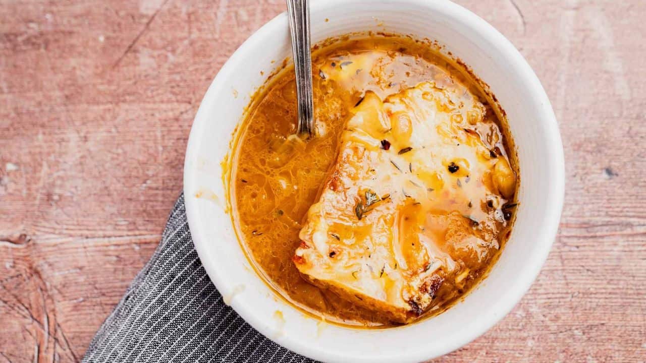 A bowl of French onion soup topped with melted cheese and bread, with a spoon resting inside the bowl.