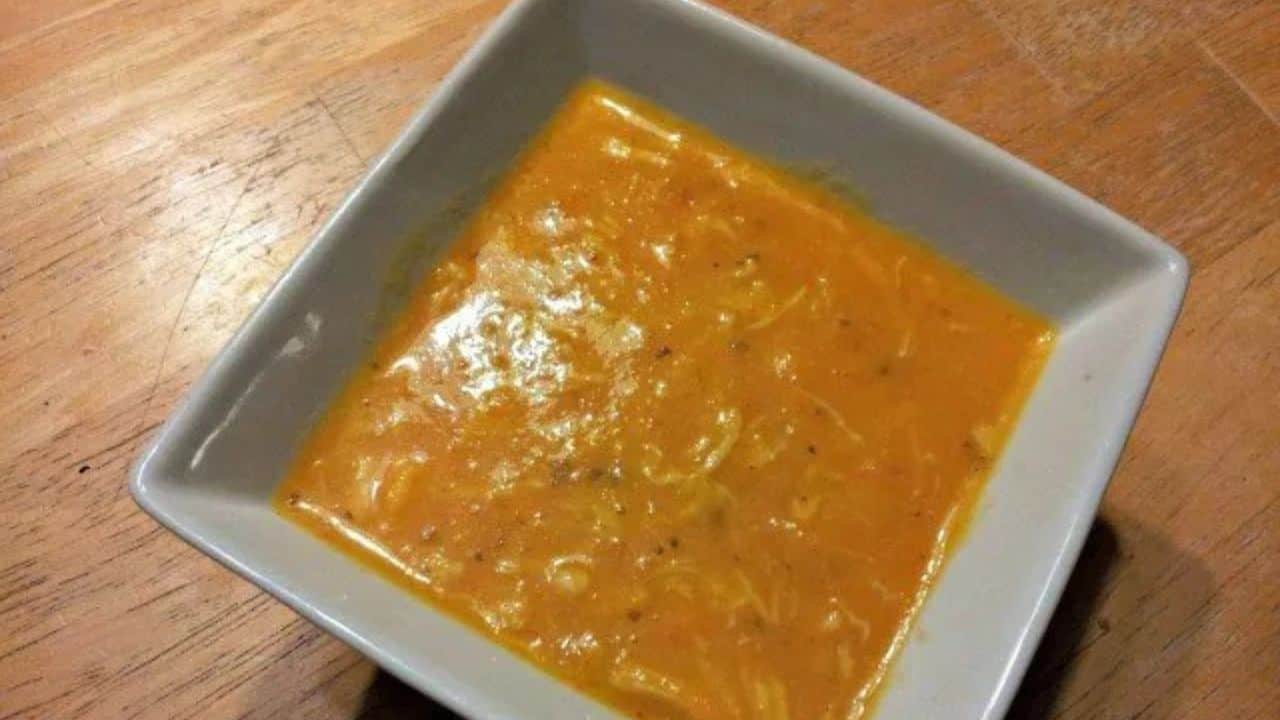 Image shows A bowl of carrot chicken soup on a wooden table.