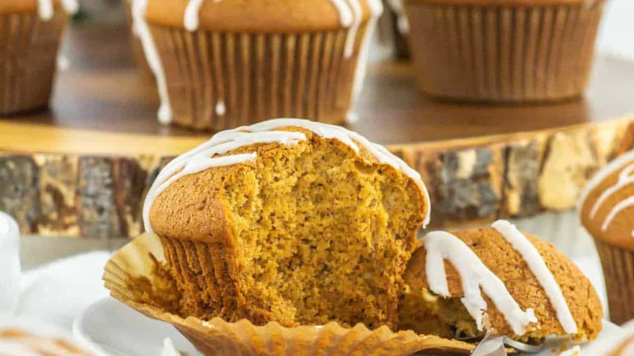A close-up of a partially eaten muffin with white icing, unwrapped from its paper liner, with whole muffins in the background.