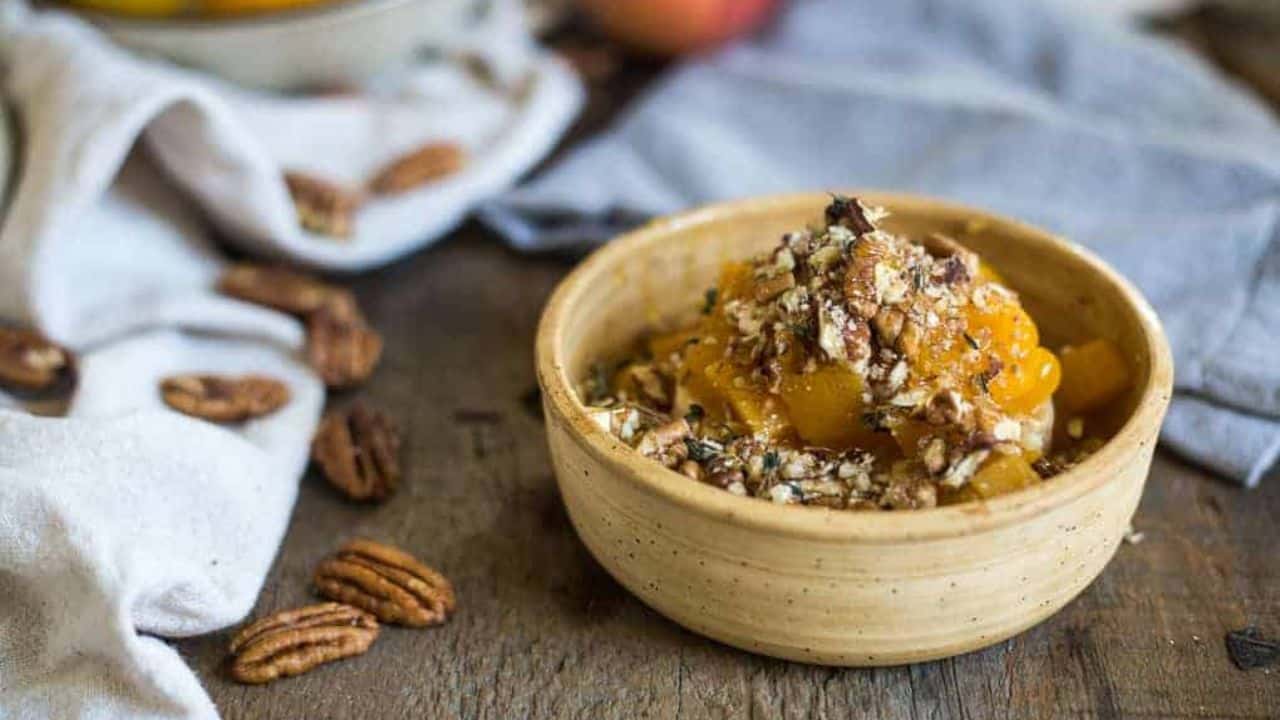 A person is dipping a piece of bread into a bowl of peach and pecan dip.