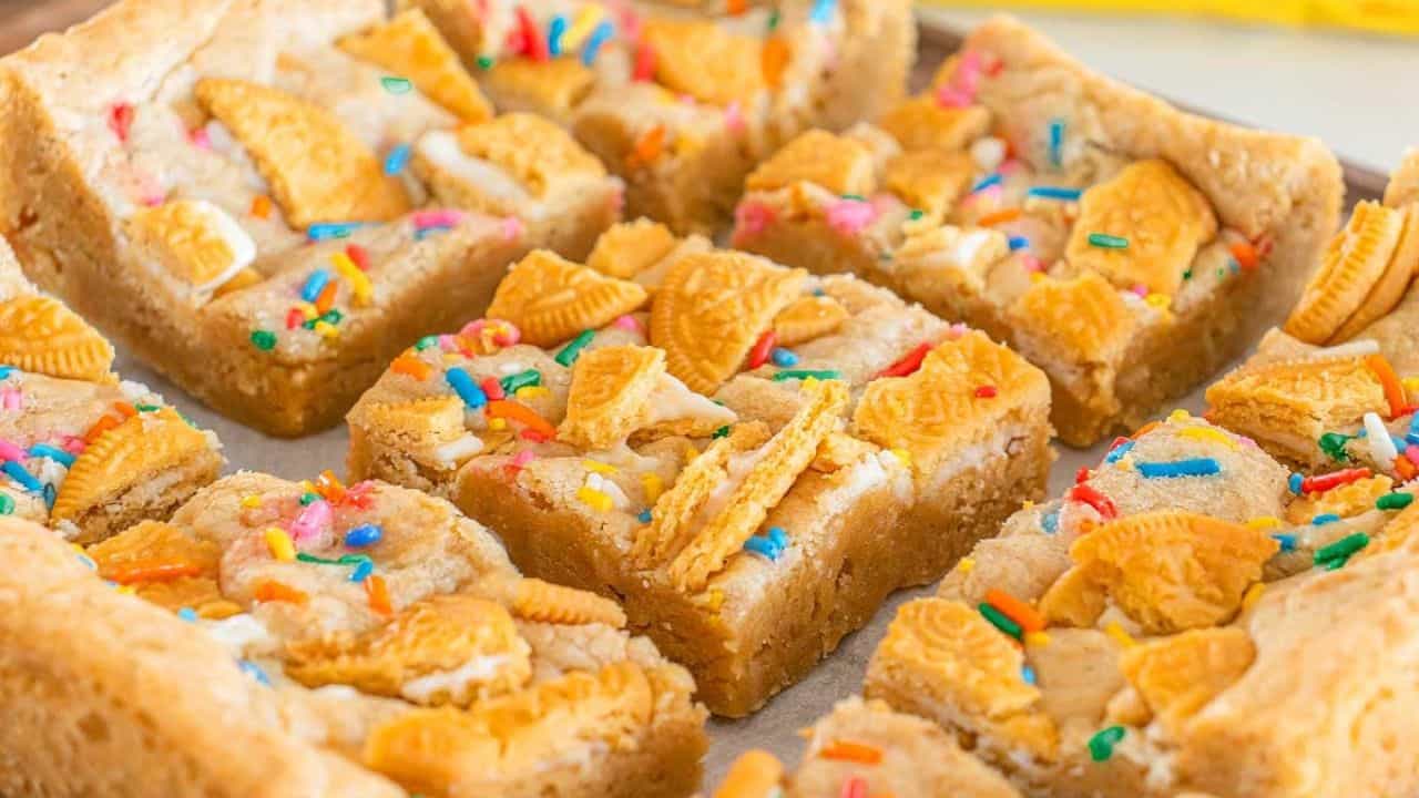 Golden Oreo cookie bars topped with broken cookie pieces and colorful sprinkles, cut into squares and arranged on a tray.