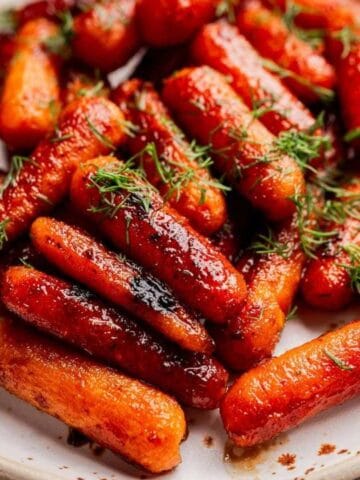 A plate of glazed carrots garnished with fresh herbs, placed on a rustic wooden table next to a striped cloth napkin.