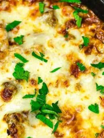A baked skillet dish topped with melted cheese and chopped fresh parsley.