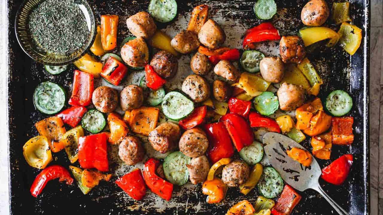 Close-up of roasted meatballs with a mix of colorful, chopped bell peppers and zucchini slices.